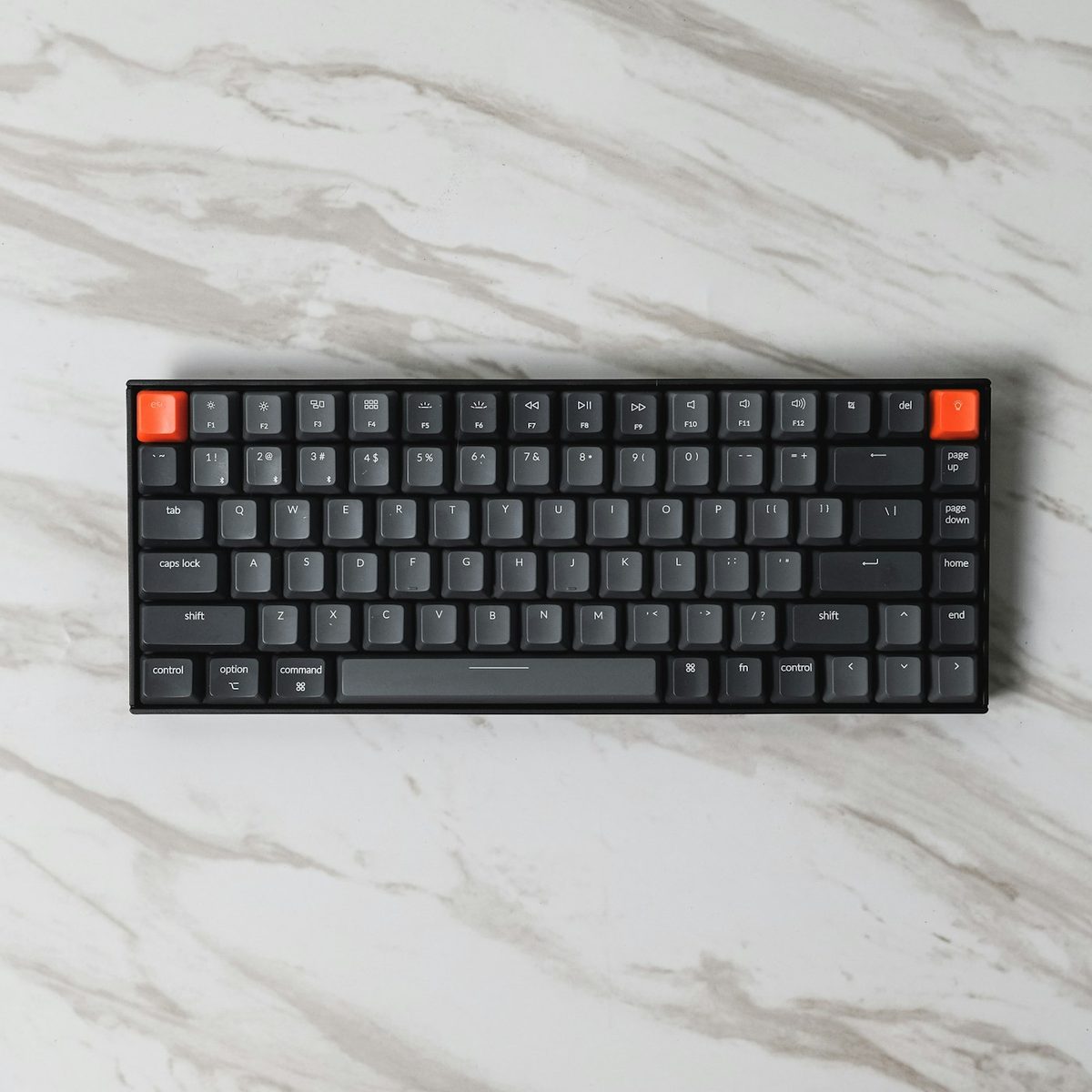 Black compact mechanical keyboard with orange accent keys on marble