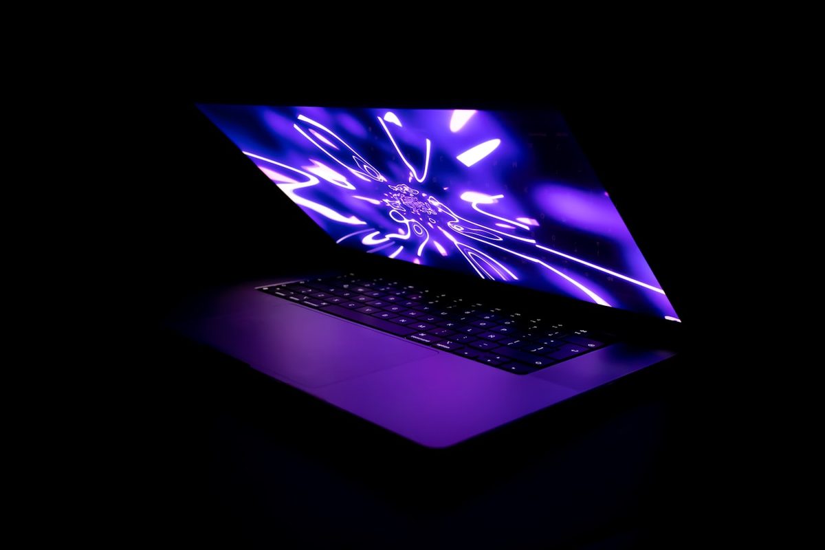 Slim open laptop glowing with a purple neon abstract wallpaper in a dark room